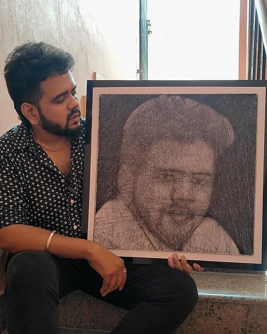 Man sitting beside his framed thread portrait