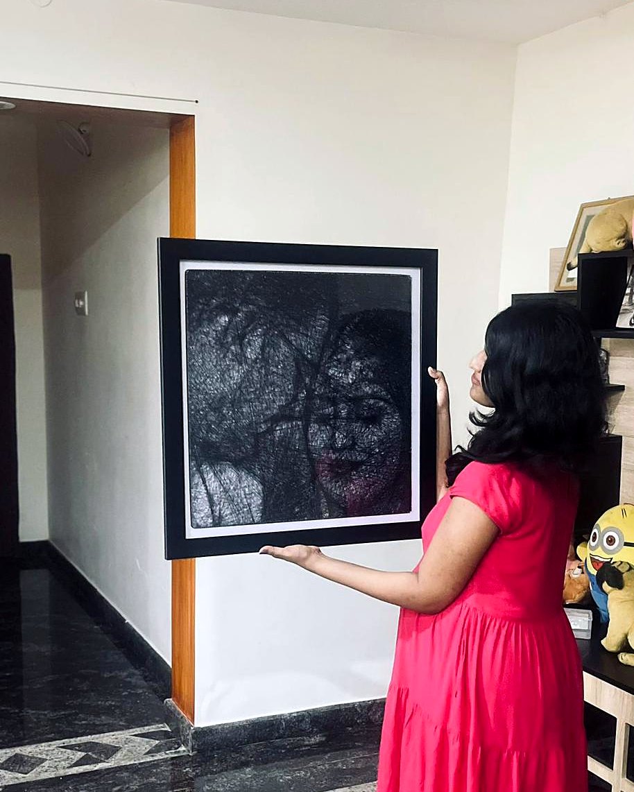 Woman hanging a framed thread portrait on her wall